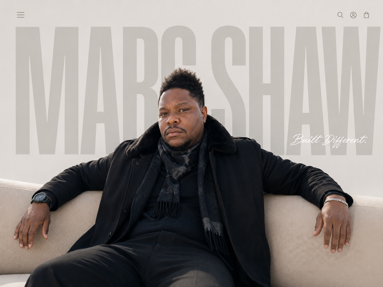 Marc Shaw seated, wearing a black fur-collared coat, beneath an oversized MARC SHAW wordmark